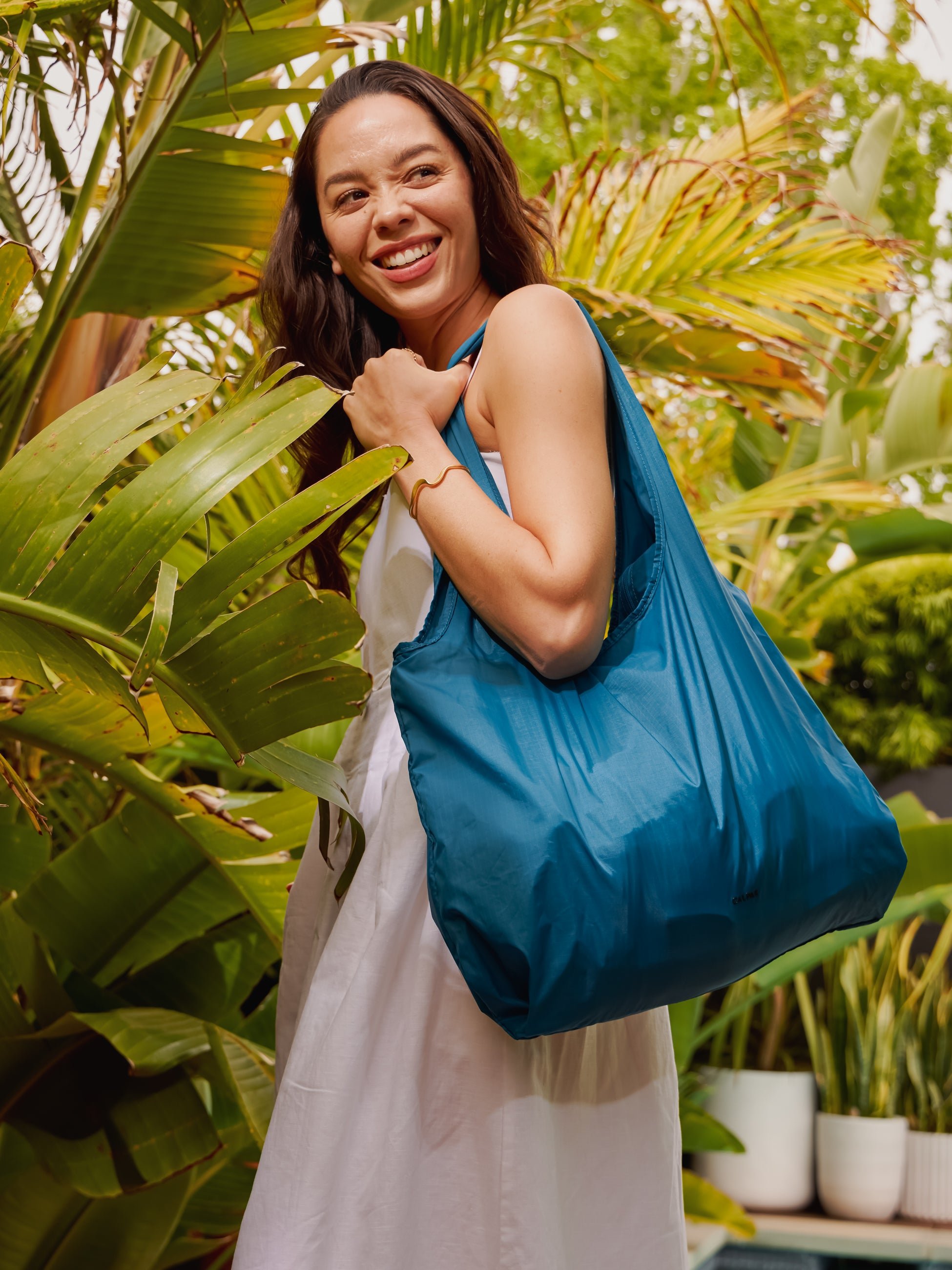 Model carrying CALPAK Compakt water resistant tote bag in lagoon blue