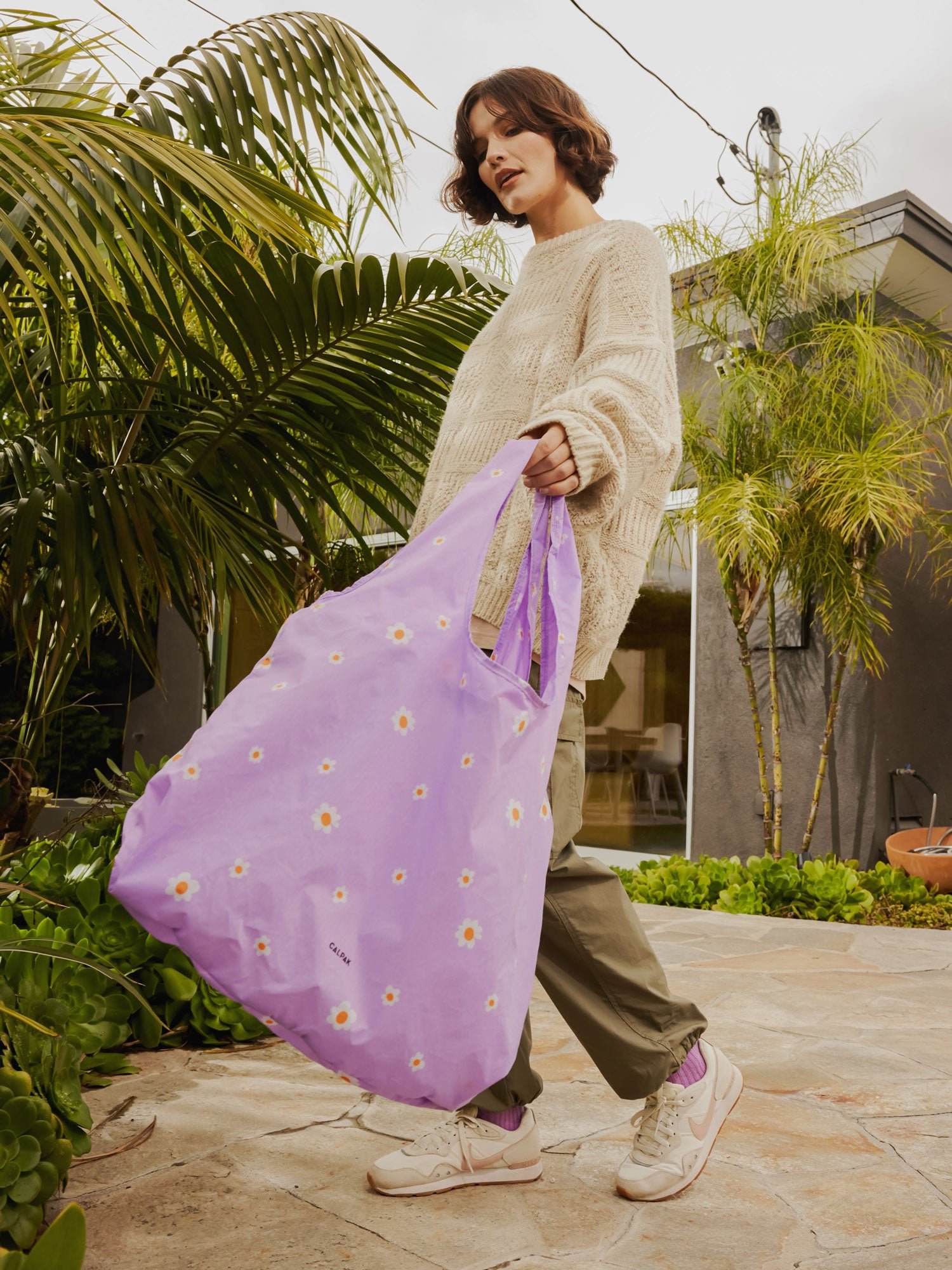 Model carrying CALPAK Compakt water resistant tote bag in purple floral print