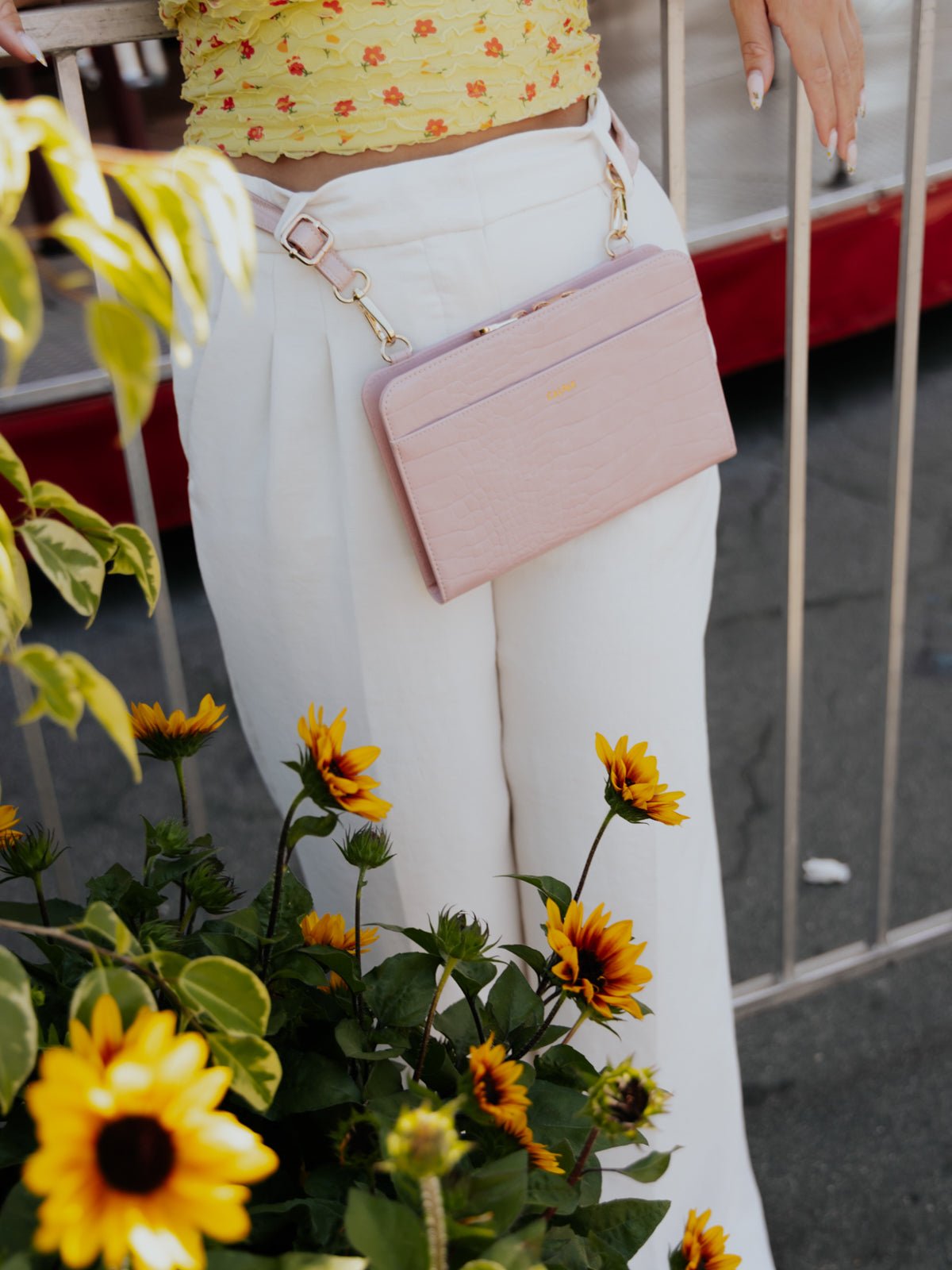 Model leaning against fence wearing pink CALPAK Croc Wallet as waist bag
