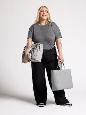 Model holding smoke gray CALPAK Haven Laptop Tote in left hand with insert in right hand; ATO2101-SMOKE