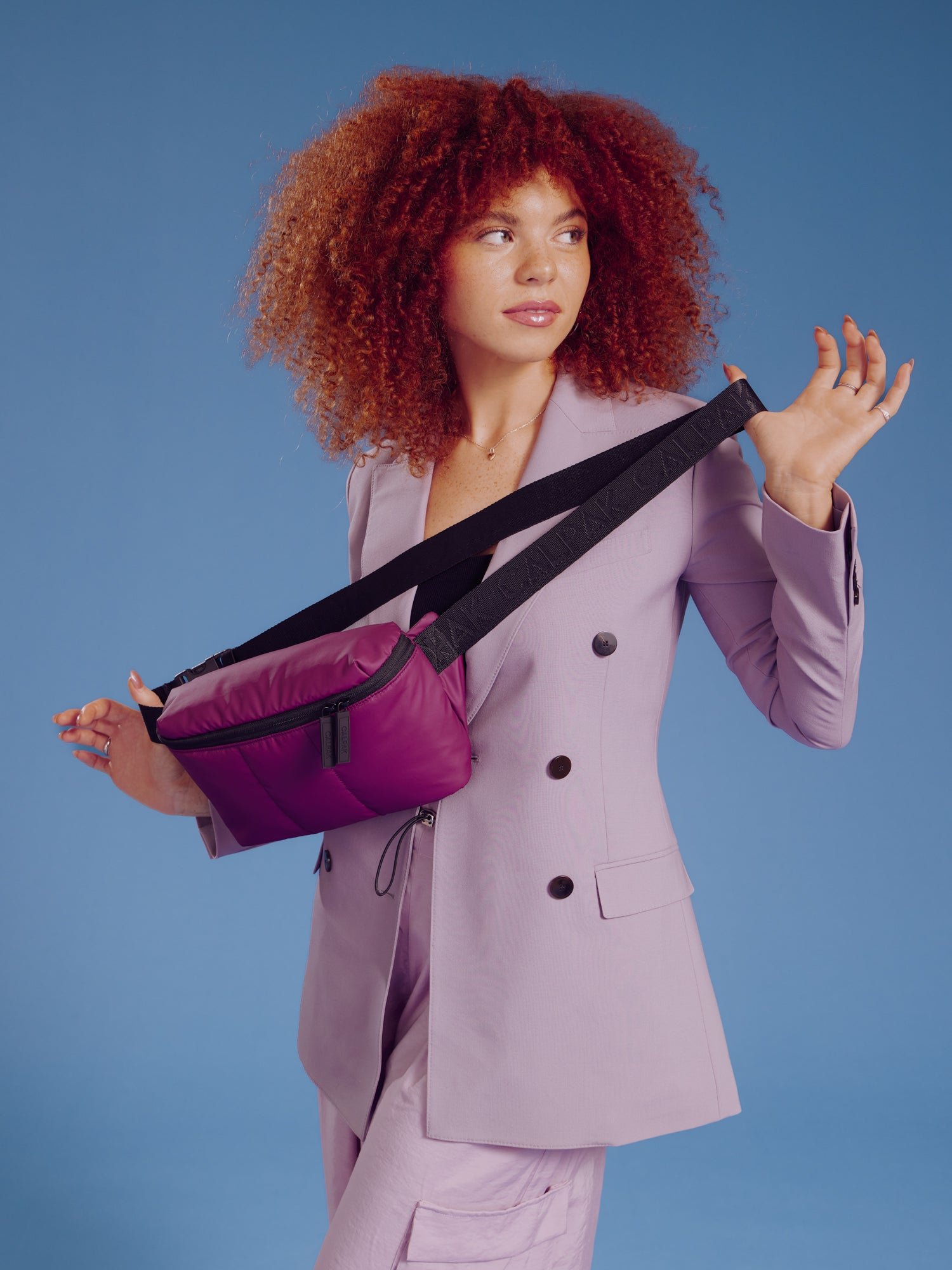 Model holding CALPAK Luka Belt Bag in plum by adjustable strap