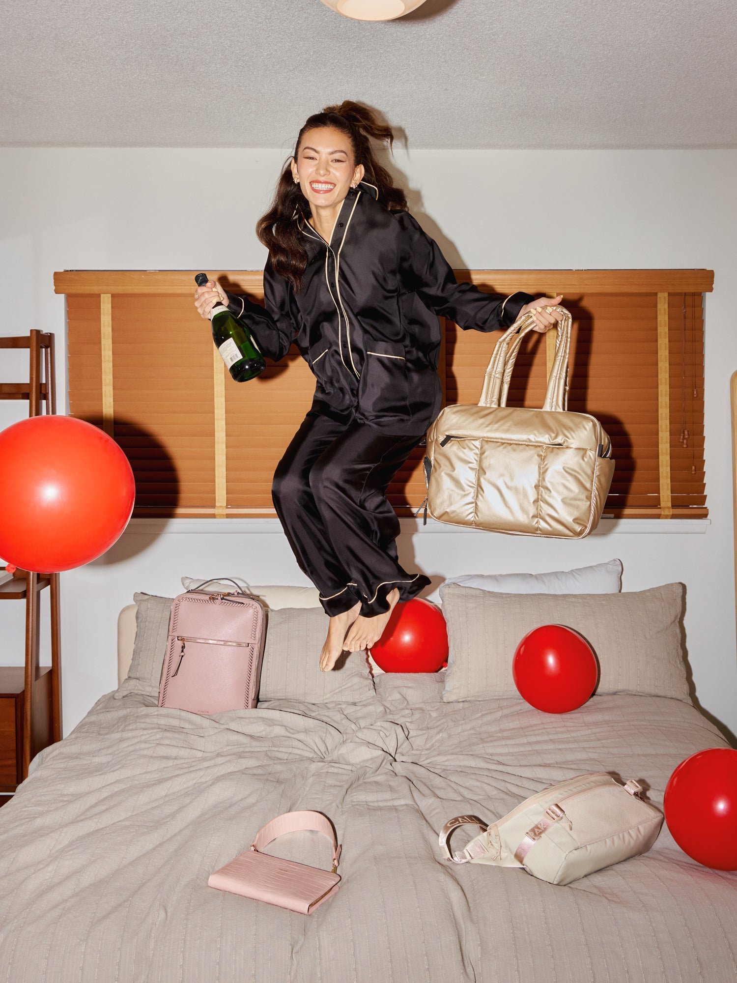 Model jumping on bed with metallic gold Luka Duffel in left hand
