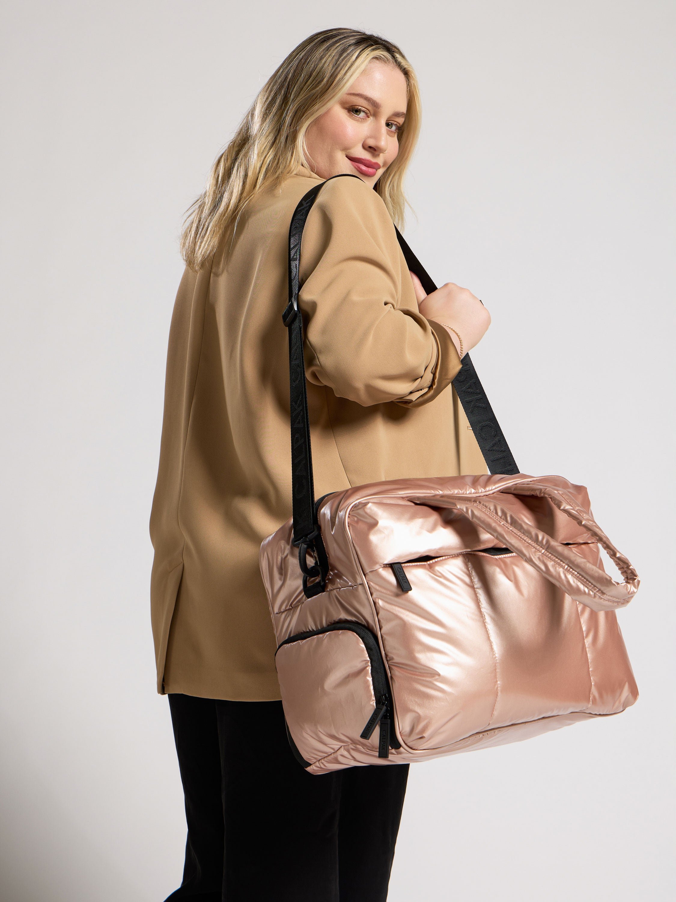 Model using detachable strap to carry rose gold Luka Duffel over shoulder