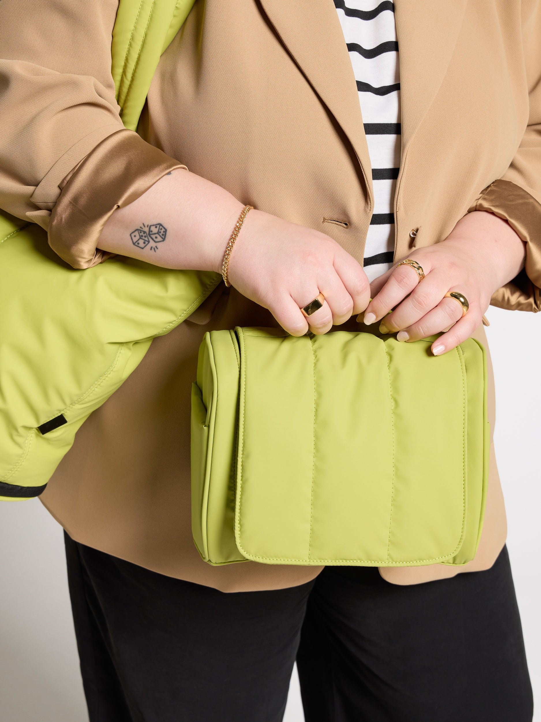 Model holding ultra-plush celery luka hanging toiletry bag with CALPAK luka expandable laptop tote bag over shoulder in celery