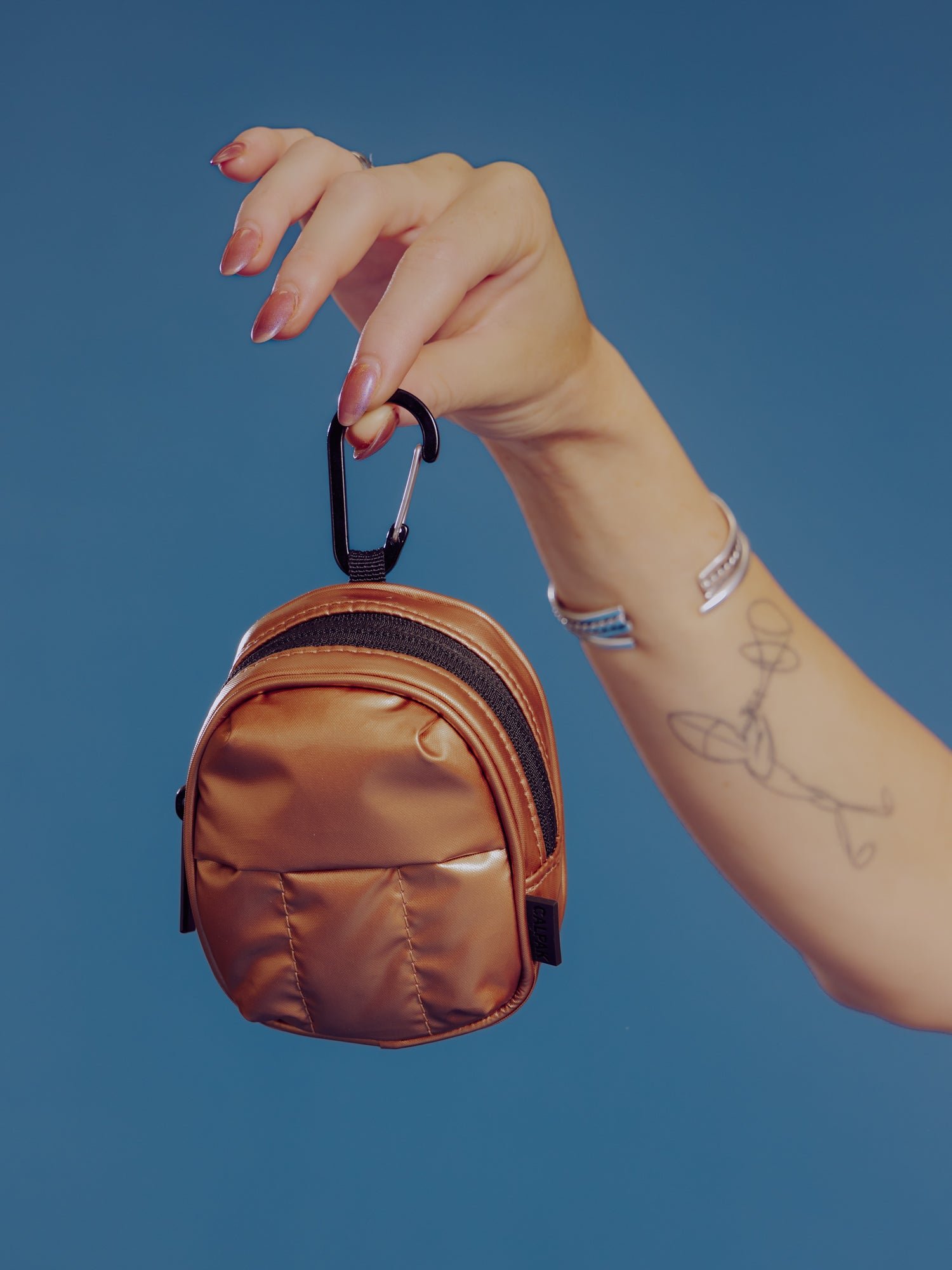 Model holding up CALPAK Luka Key Pouch in copper by the carabiner clip