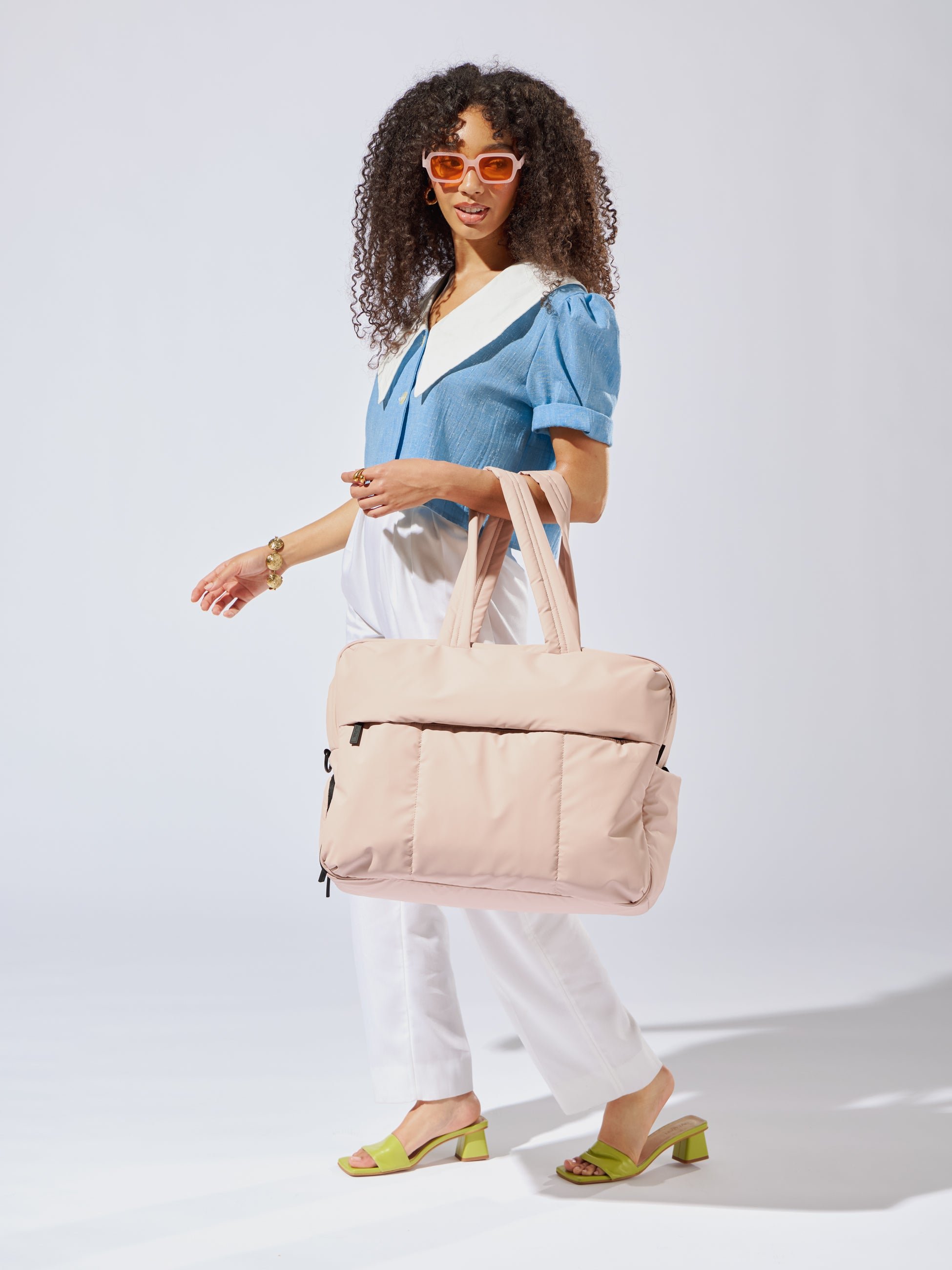 Model carrying CALPAK Luka large duffle bag with padded should straps and zippered front pocket in light pink