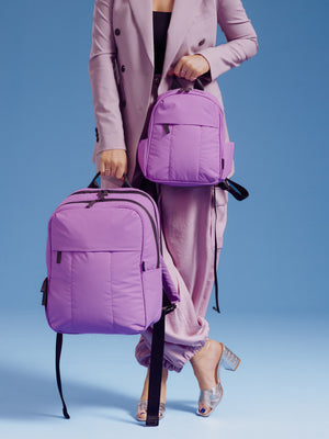 Model holding the CALPAK Luka Mini Backpack and CALPAK 15 inch Laptop Backpack in lavender lilac for size comparison; BPM2201-LILAC