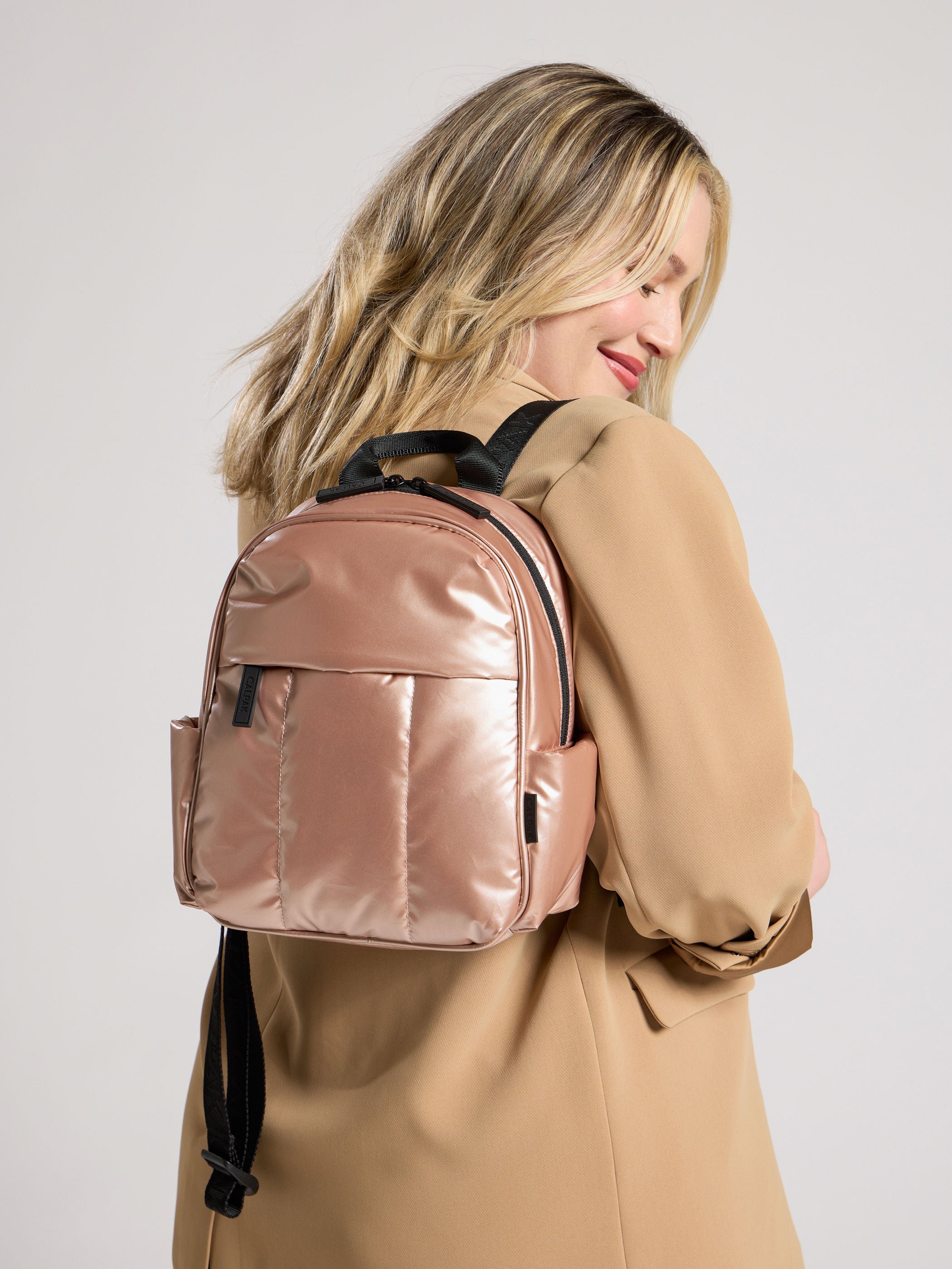 Model wearing CALPAK Luka Mini Backpack on back in metallic pink rose gold