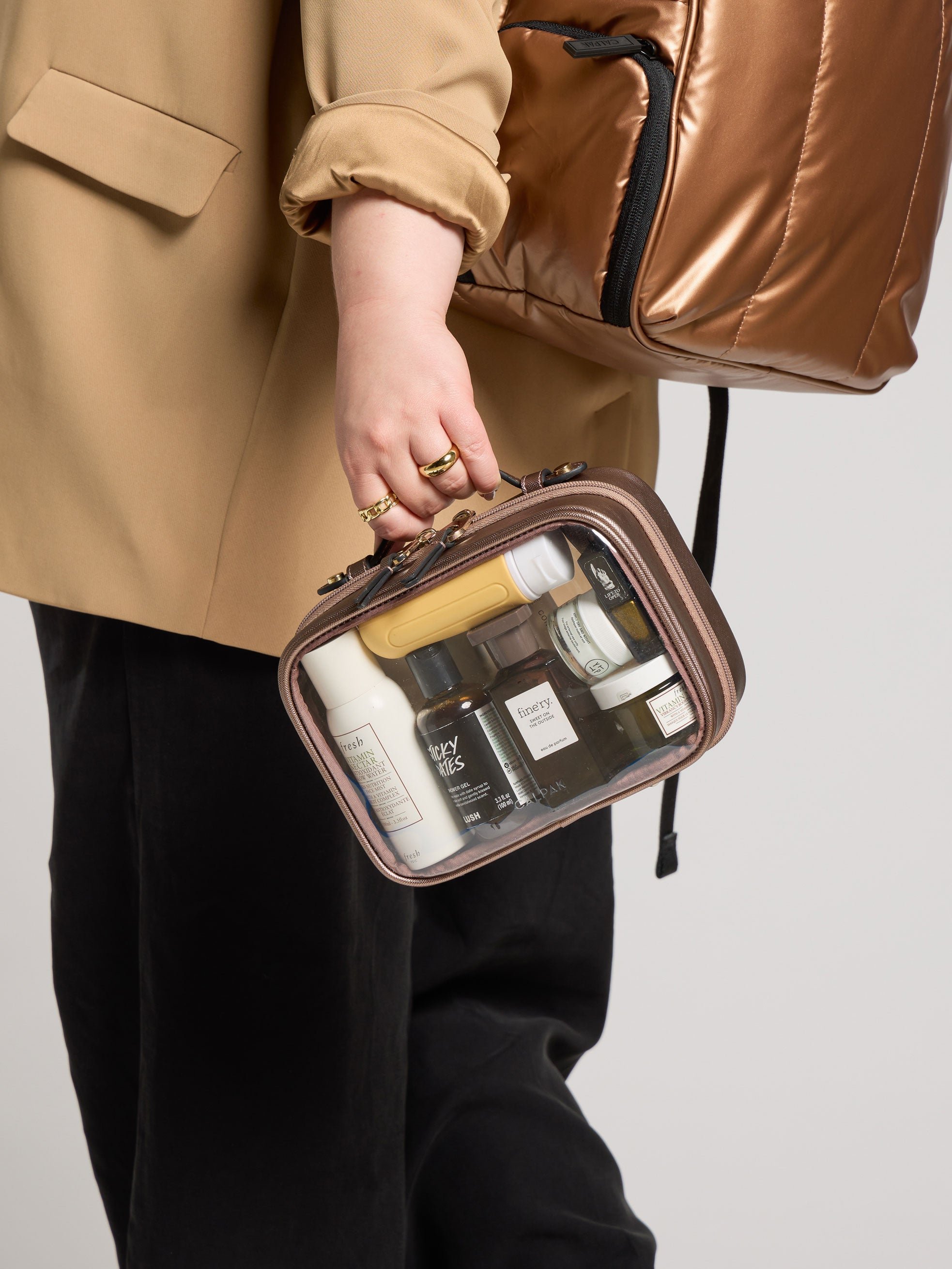 Model holding CALPAK Small Clear Cosmetic case in bronze