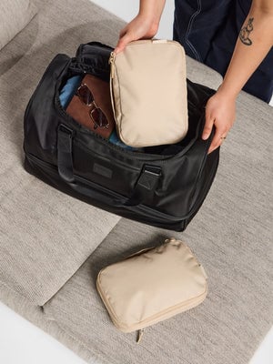 Model placing oatmeal CALPAK Small Compressing Packing Cubes in Stevyn Duffel Bag with Shoe Compartment;  PCS2301-OATMEAL