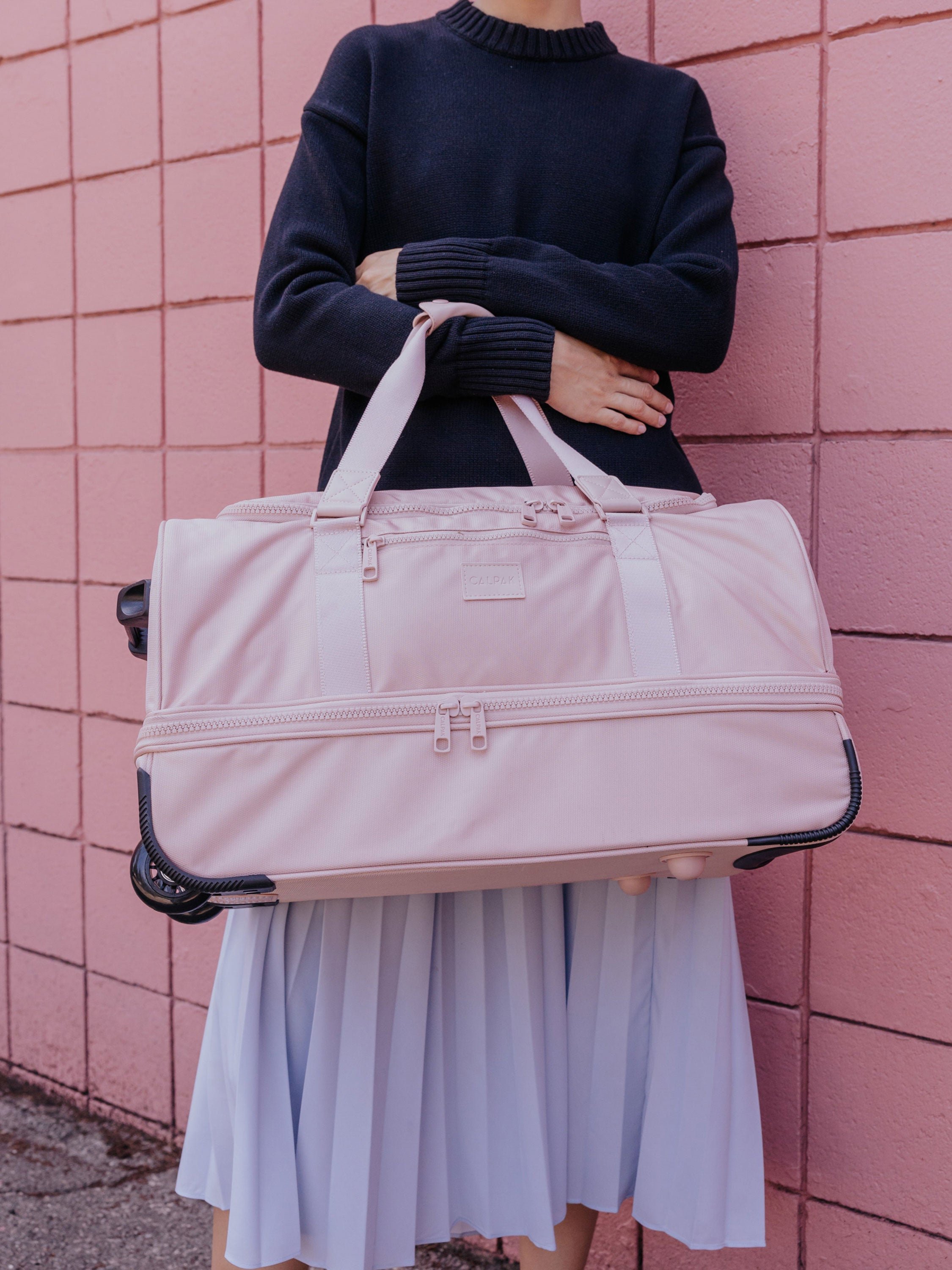 CALPAK Stevyn Rolling Duffle carried with dual handles in pink sand