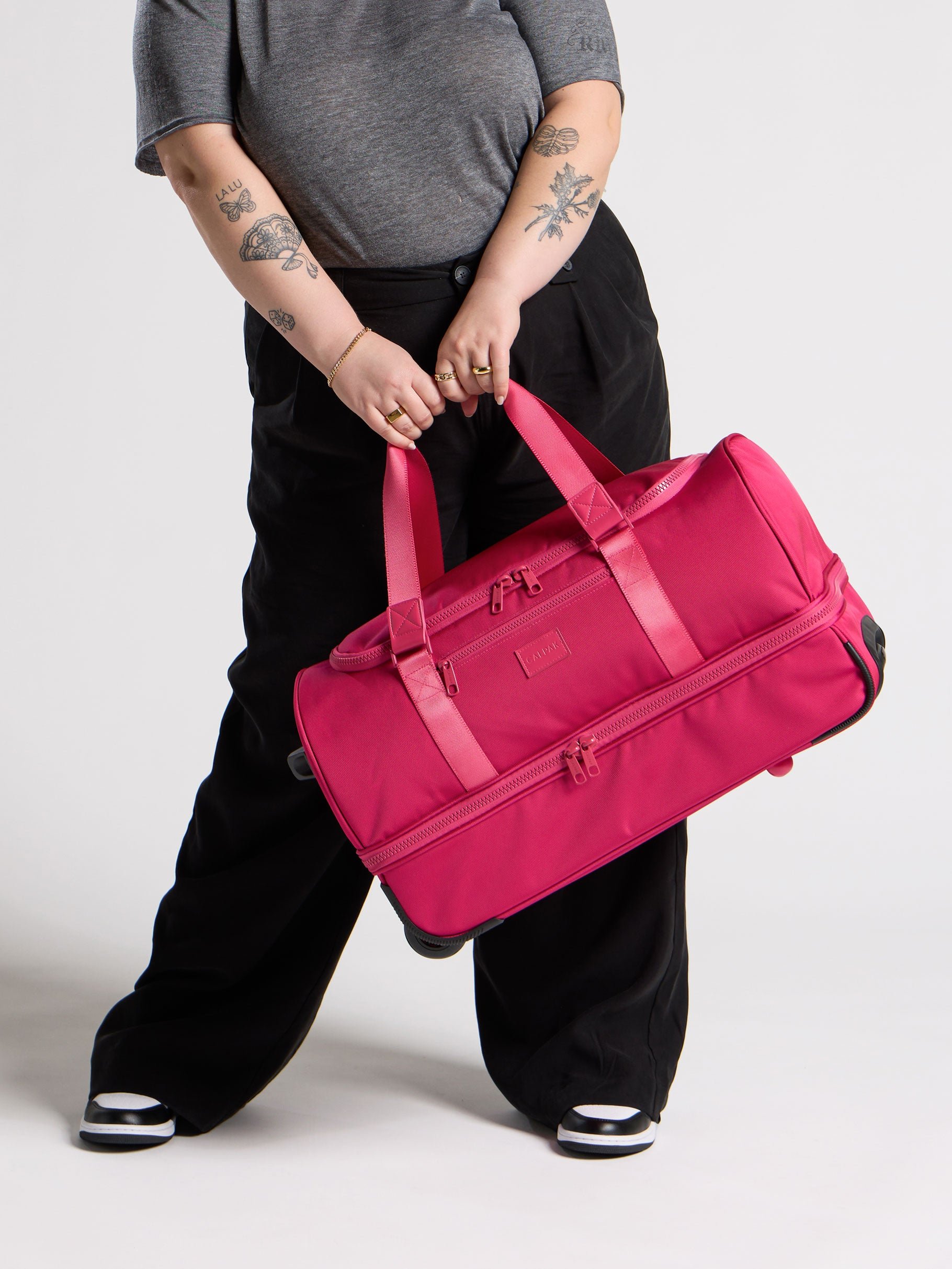 Model holding CALPAK Stevyn Rolling Duffel with shoe compartment in dragonfruit