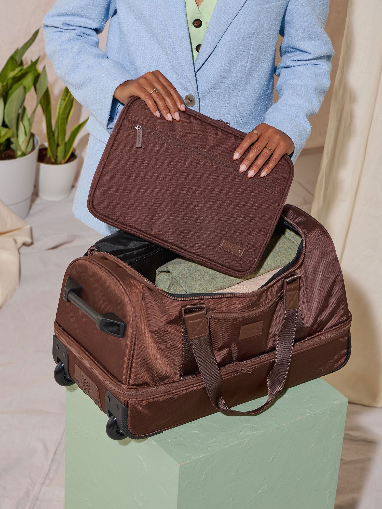Model packing laptop case in CALPAK Stevyn Rolling Duffel bag with dual handles in walnut brown