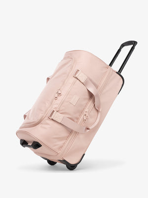 CALPAK Stevyn Rolling Duffel side view with top handle extended in pink sand; DSR2201-PINK-SAND