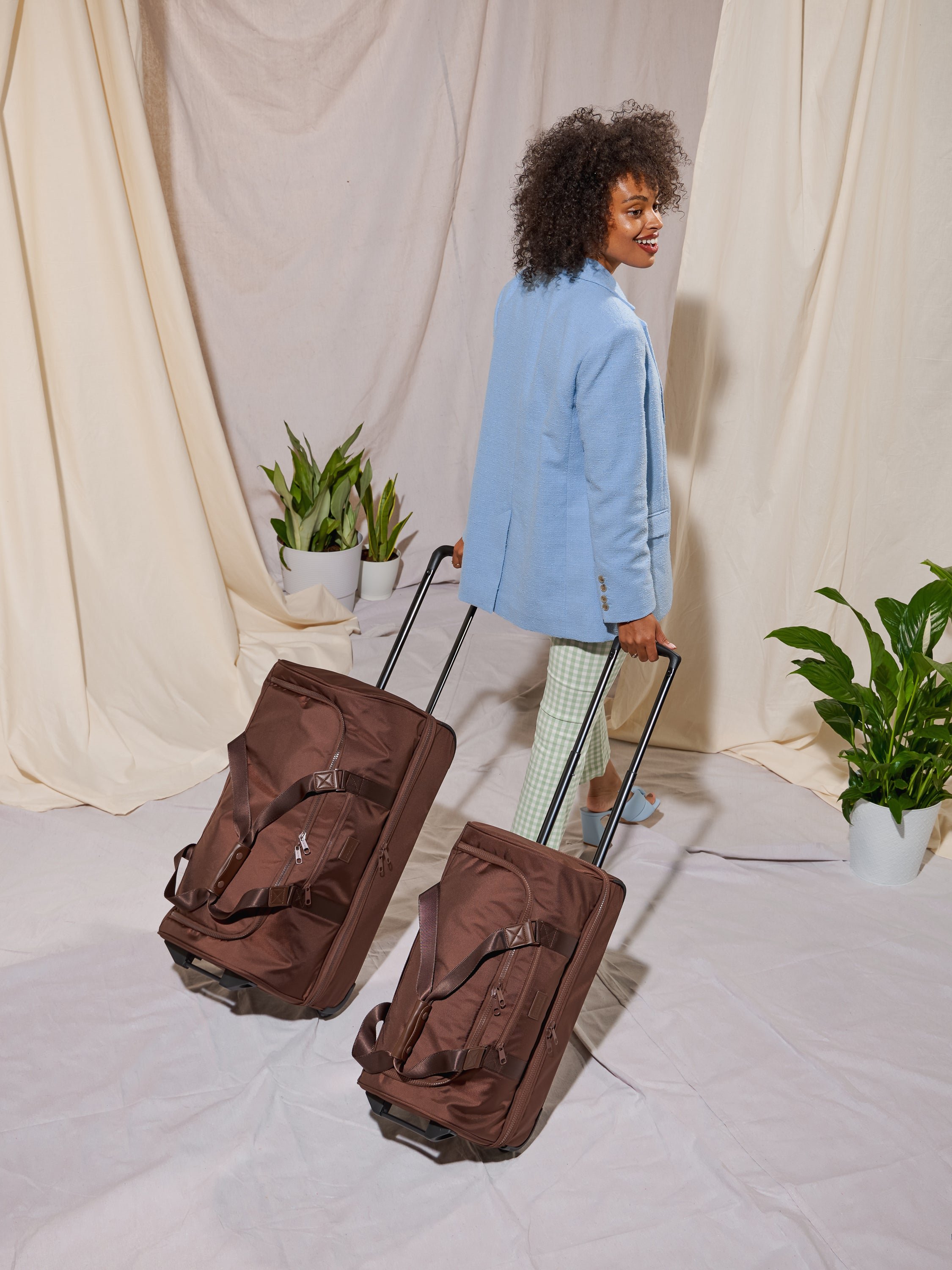 Model with CALPAK Stevyn Rolling Duffle and Large Rolling Duffel with handle extended in brown