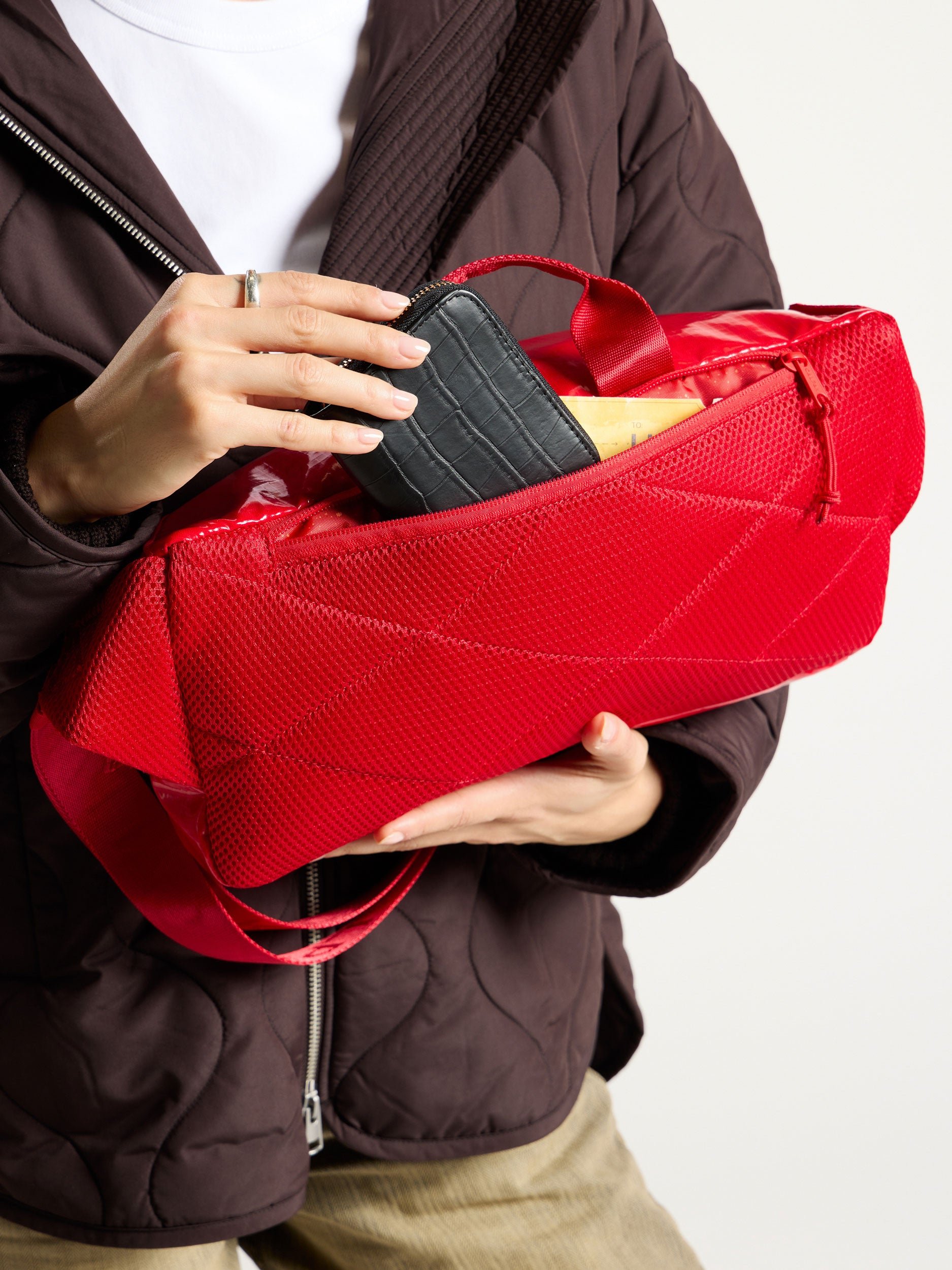 Model placing personal items within back pocket of CALPAK Terra Sling Bag in flame