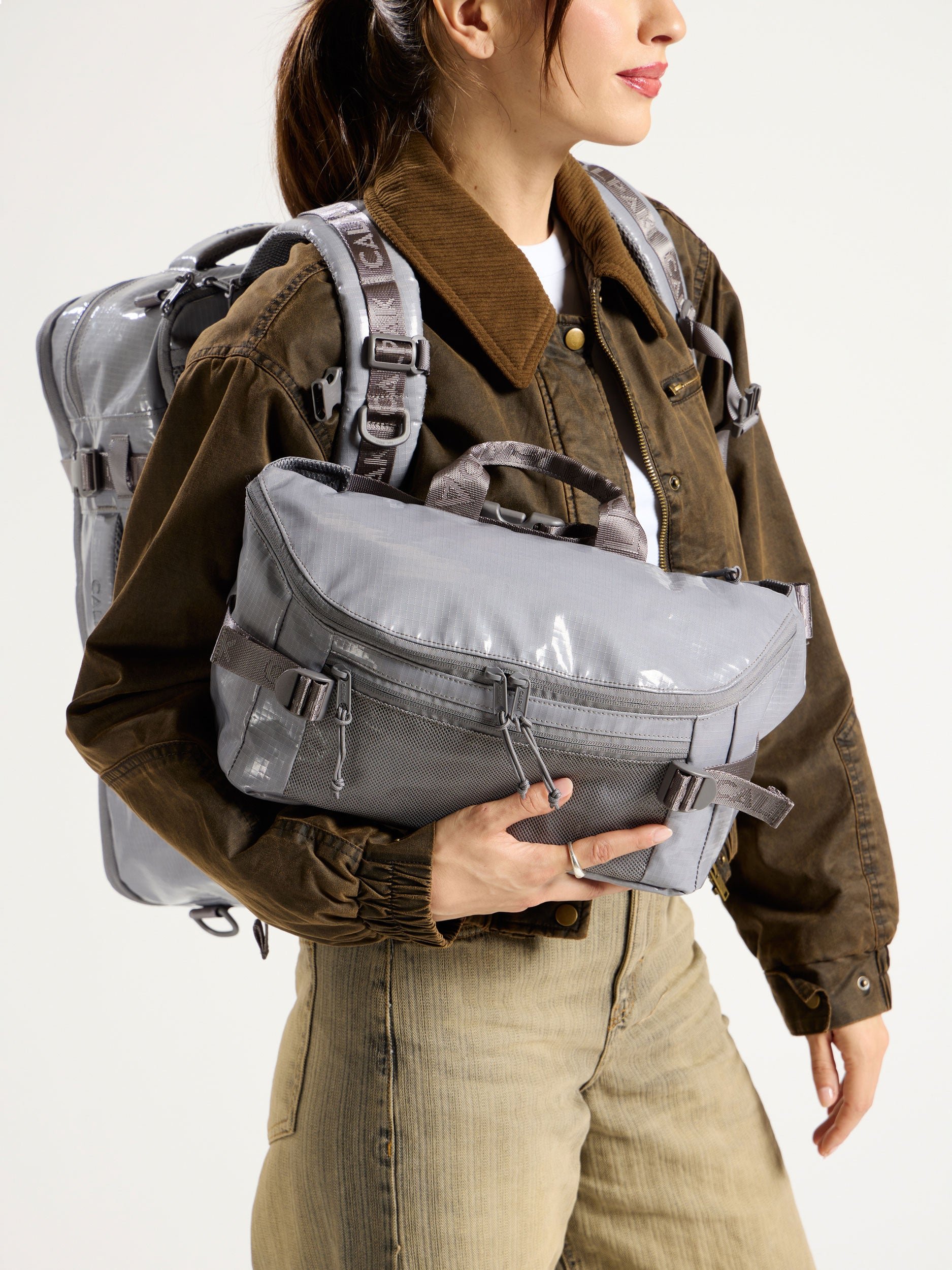 Model wearing CALPAK Terra 26L Laptop Backpack Duffel while holding gray Terra Sling Bag in arm