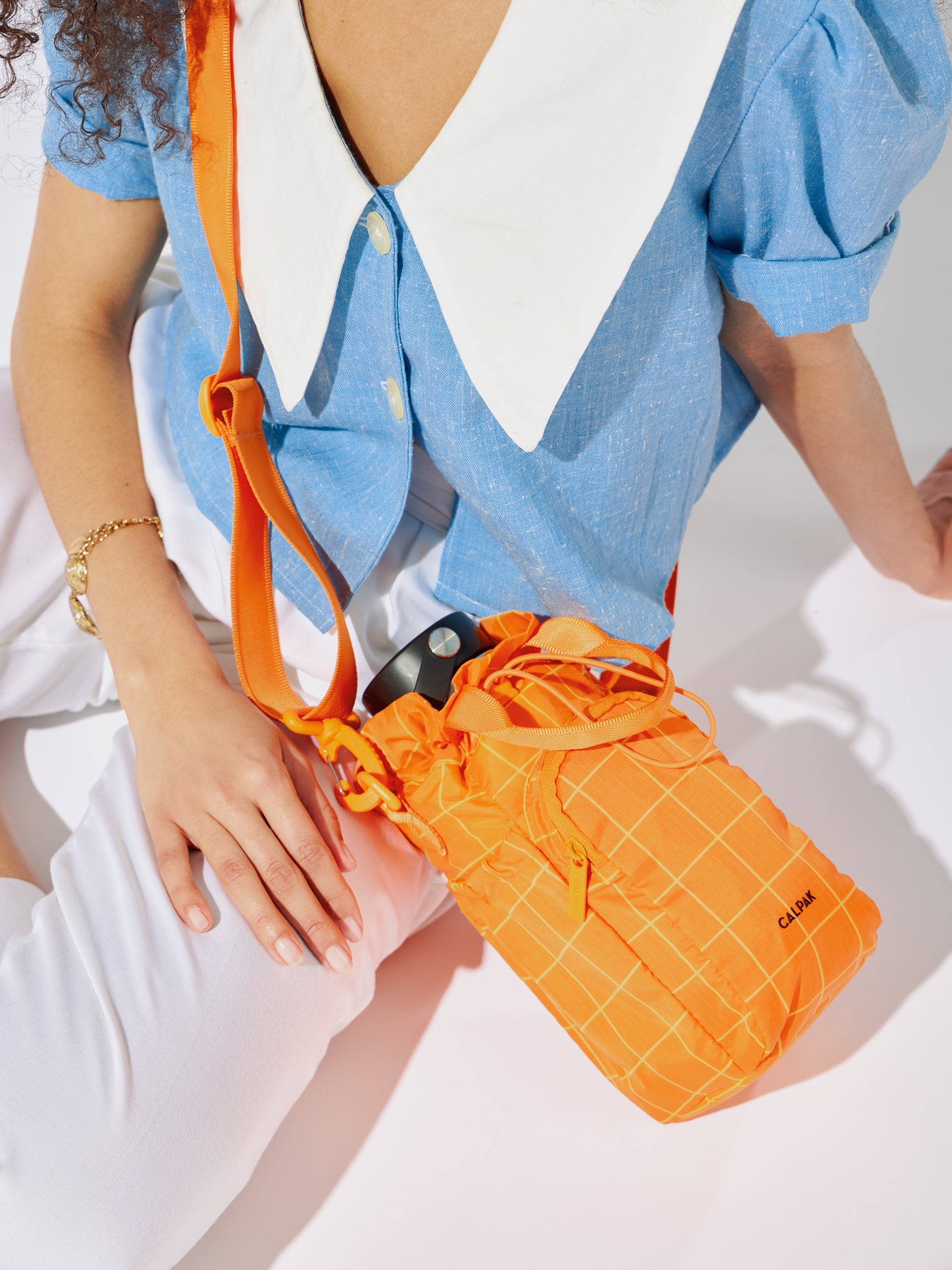 Model carrying CALPAK Water Bottle Holder with detachable sling and zipped front pocket in orange grid