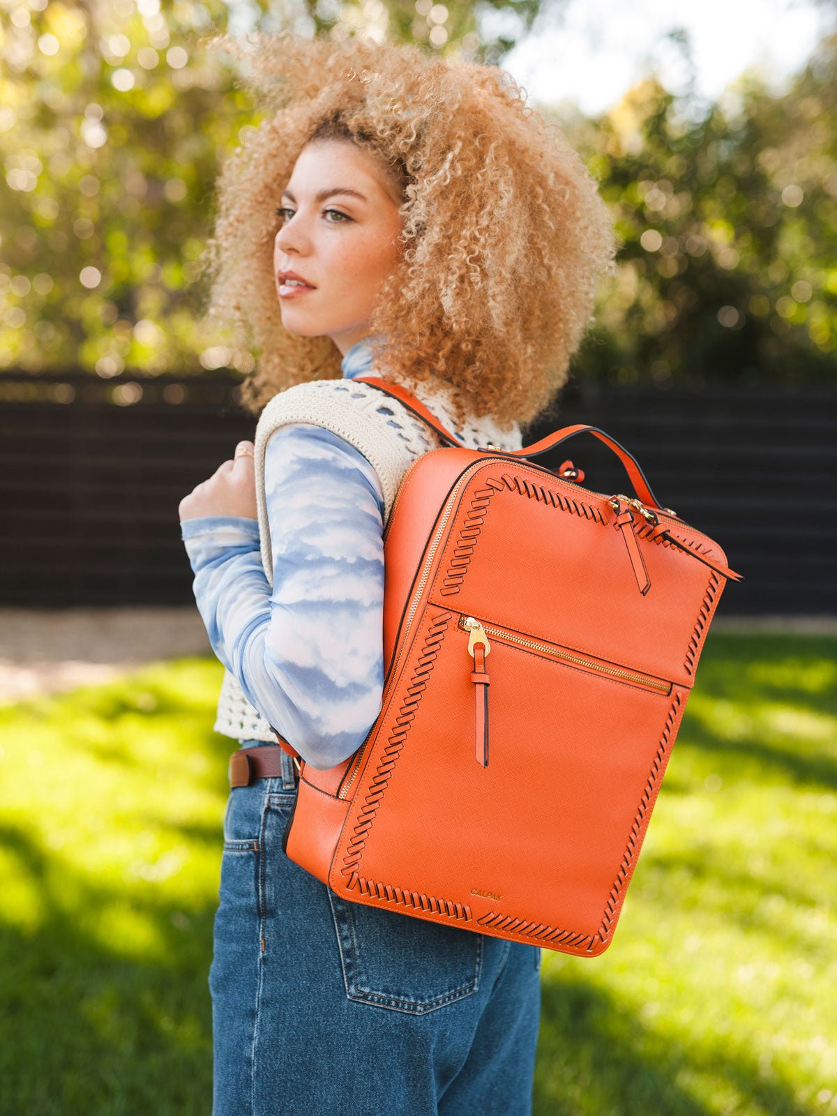 female model carrying Kaya laptop backpack in orange papaya