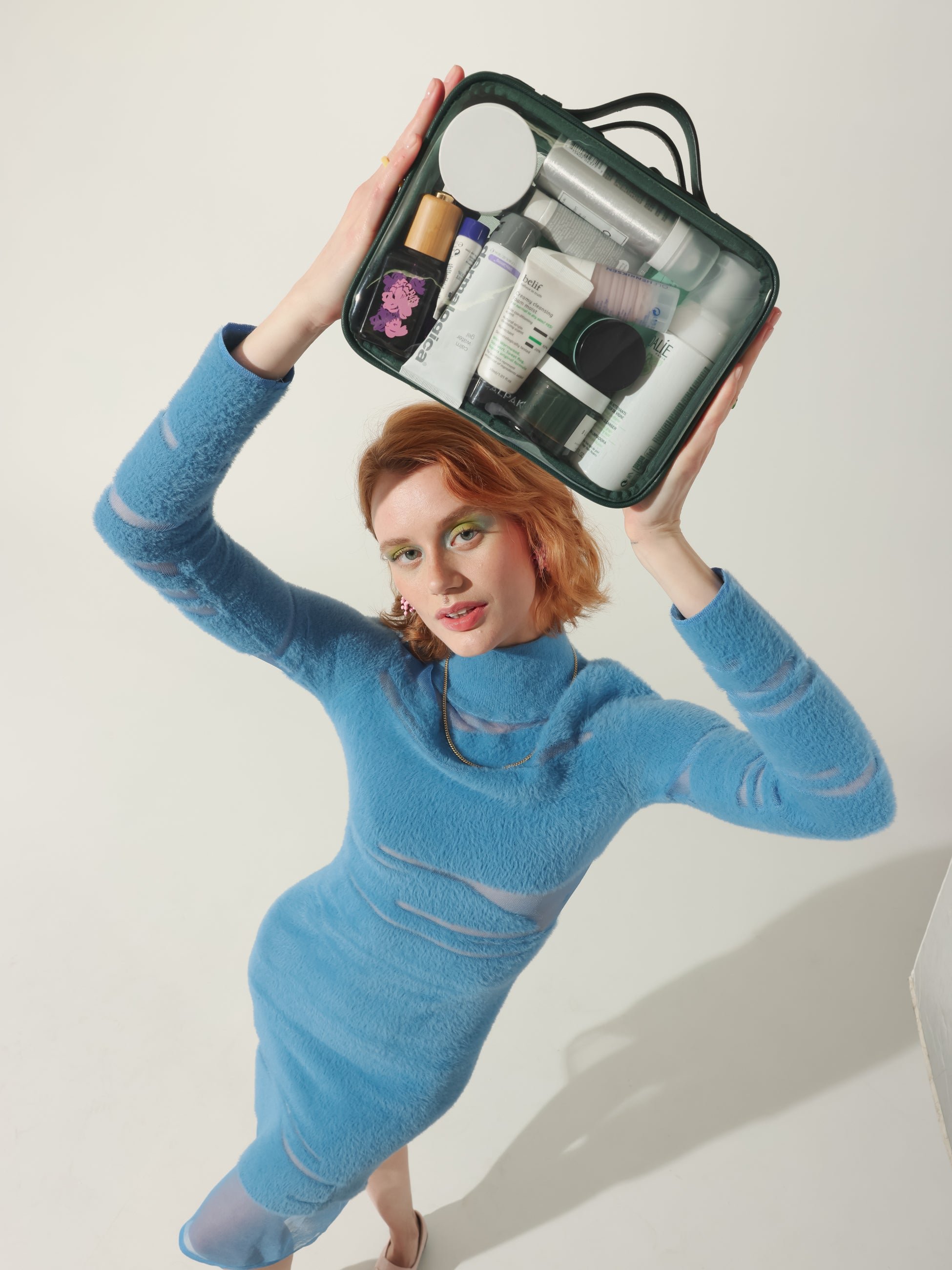 Model holding CALPAK medium transparent makeup case with top handles in emerald