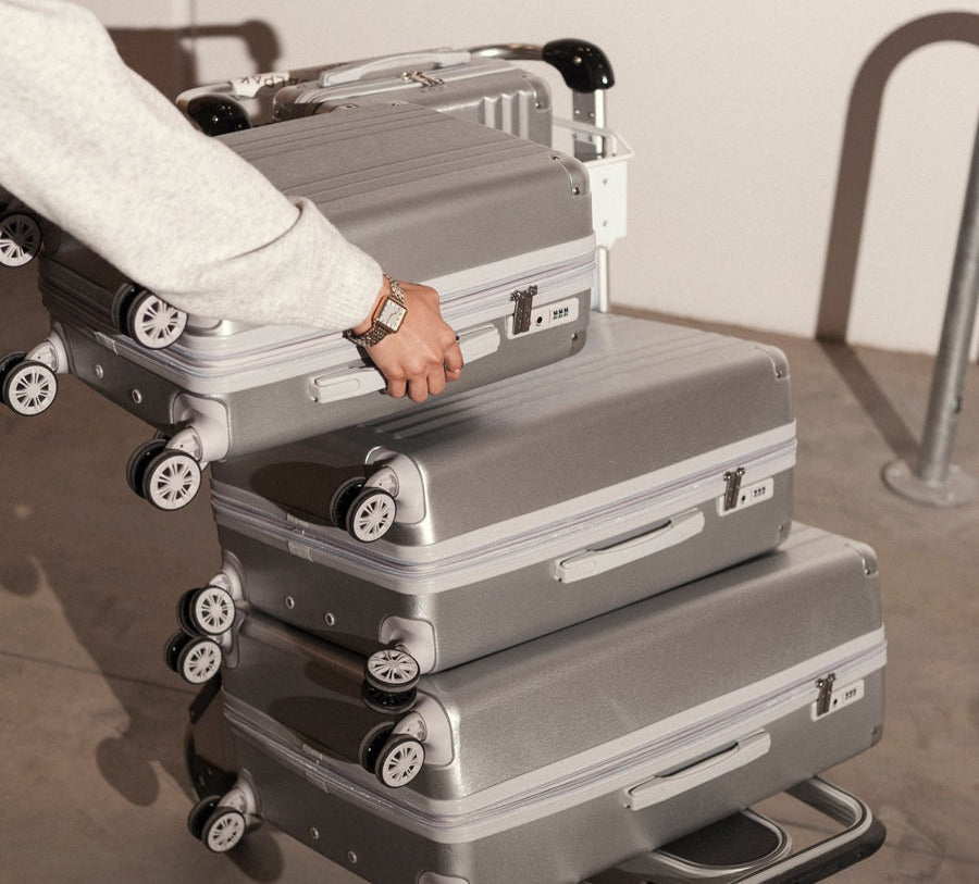 Model putting Ambeur Carry-On, Medium, Large in Silver on a cart
