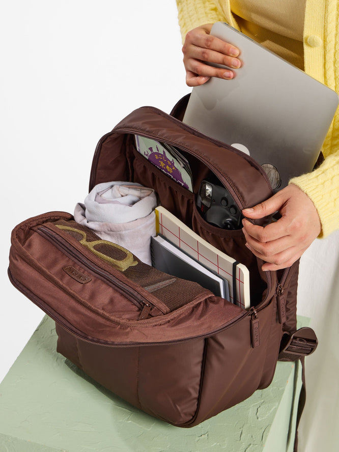 Model placing laptop into CALPAK Luka 15 inch laptop backpack in brown