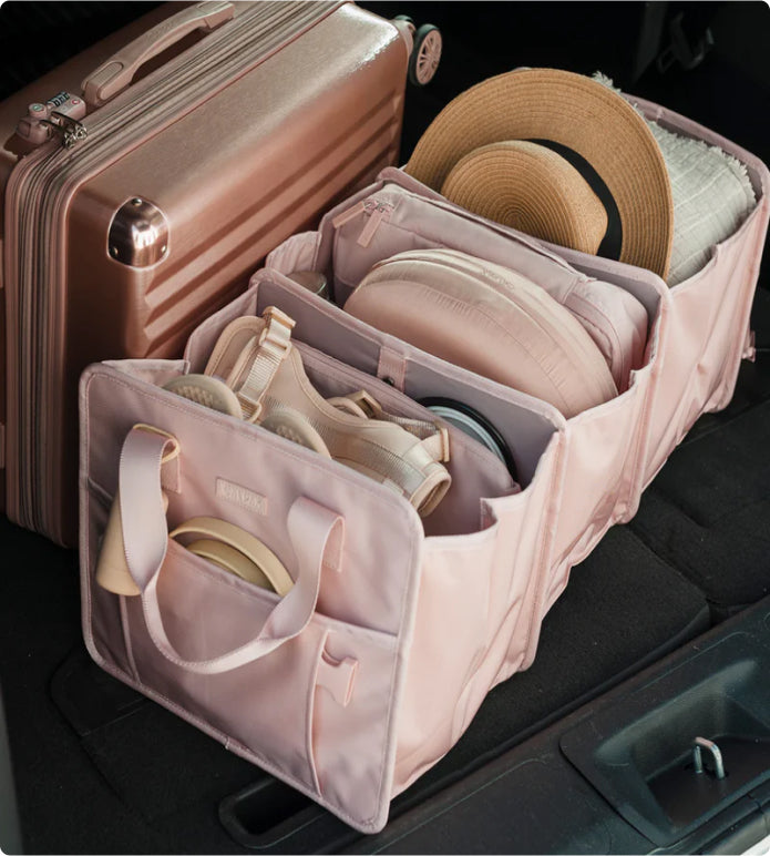 CALPAK pink car organizer packed with hat packing cubes and blanket in the back of a car trunk