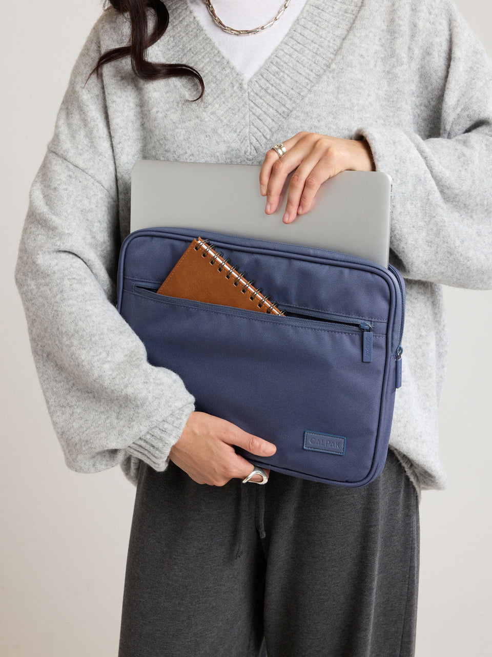 Model carrying blue padded laptop sleeve placing laptop in with notebook stored in the front zippered compartment