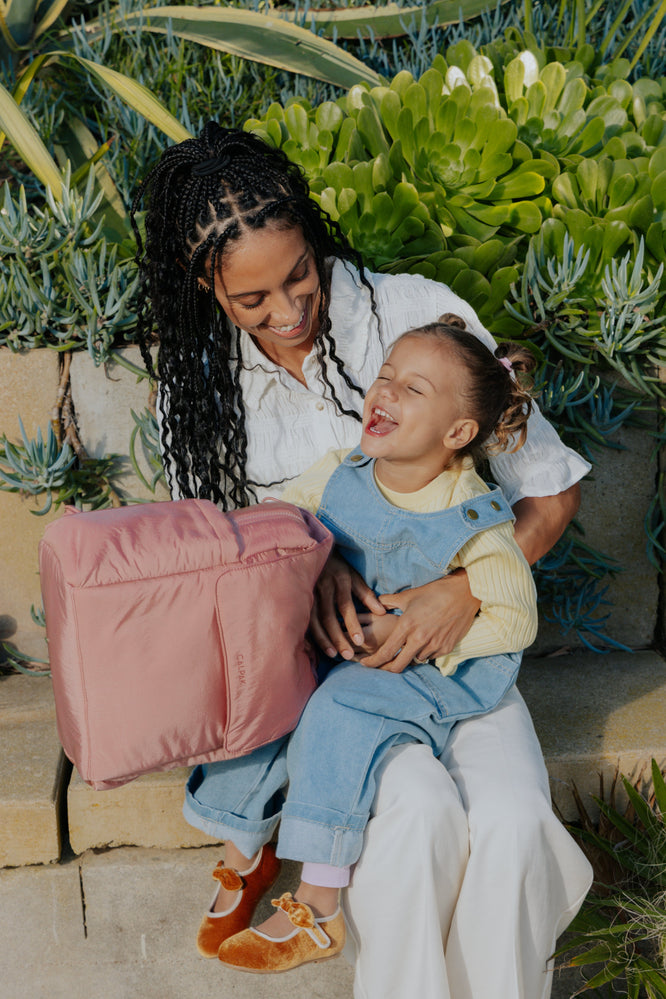 Mom with toddler on her lap while holding a CALPAK Diaper backpack in pink 