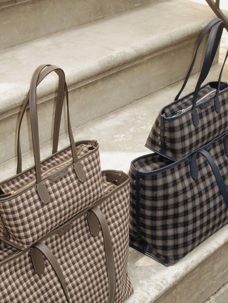 Two plaid CALPAK Colette tote bags with dark blue leather handles and trim, displayed on light stone steps.
