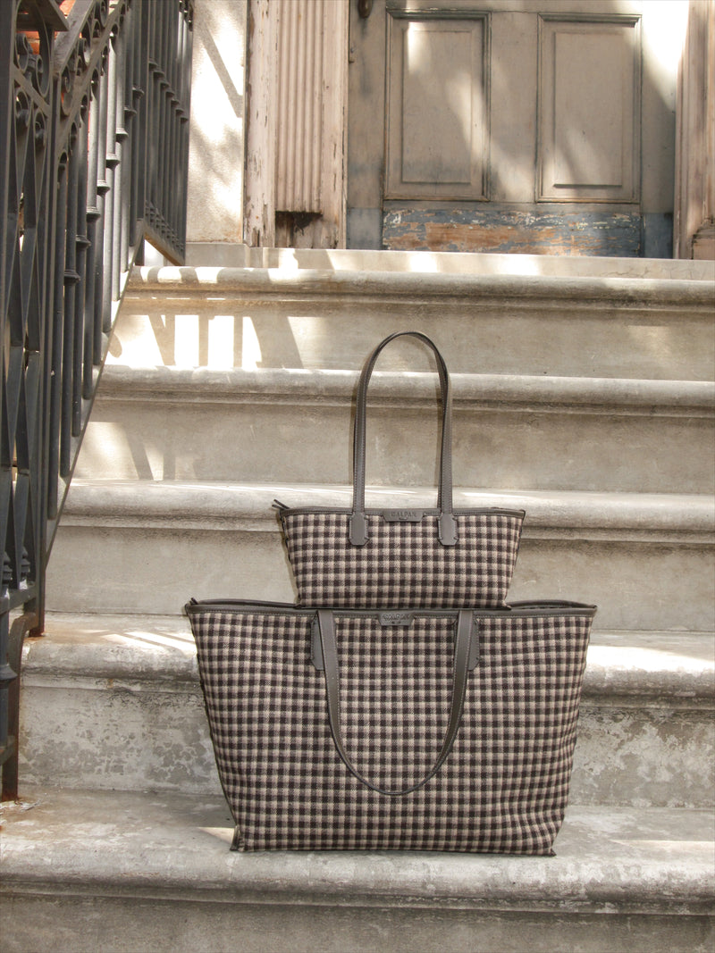 Two black and beige gingham CALPAK flannel tote bags, one small and one large, displayed on concrete steps in front of a building entrance.