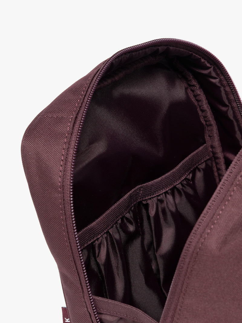 Closeup of the inner compartments of Dark burgundy Dark Cherry color of the CALPAK Everything Cube organizer with a top handle, a front zippered pocket, and a textured mesh lower panel, shown against a plain white background