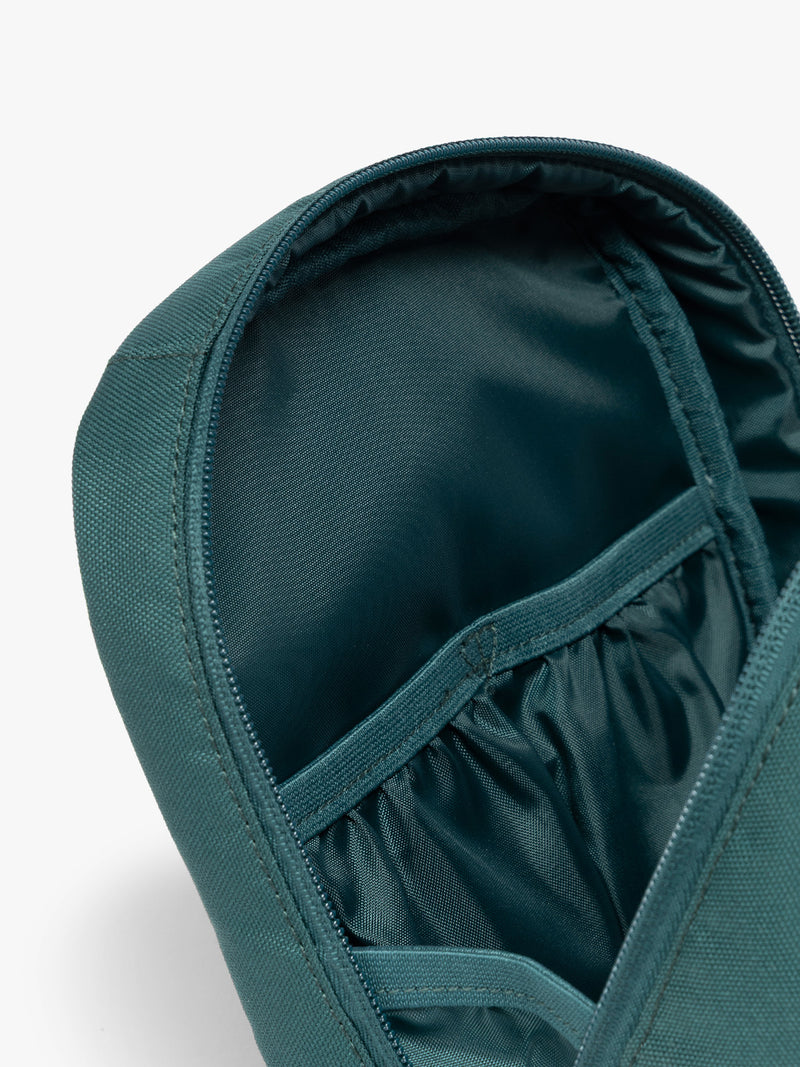 Close up of compartments in the dark teal green Kale CALPAK Everything Cube organizer with a top handle, a front zippered pocket, and a textured mesh lower panel, shown against a plain white background
