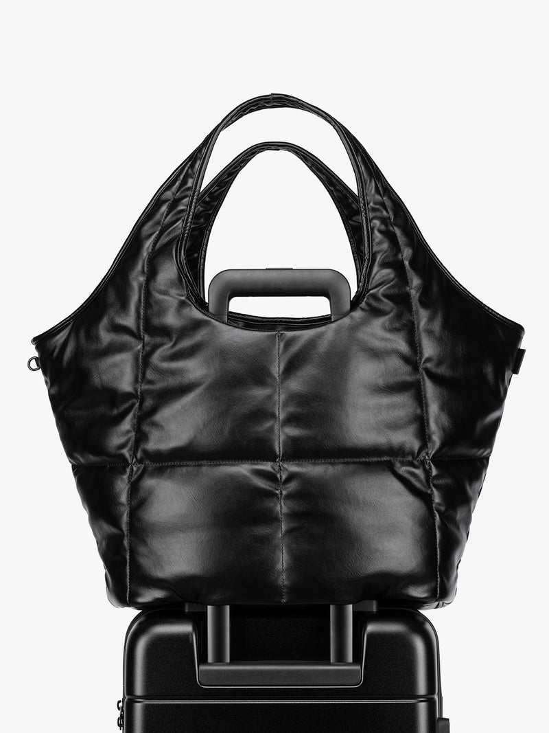 Luggage trolley sleeve feature of the Black quilted puffer CALPAK Luka Everything Tote Bag with a smooth finish and double shoulder straps, shown against a plain white background