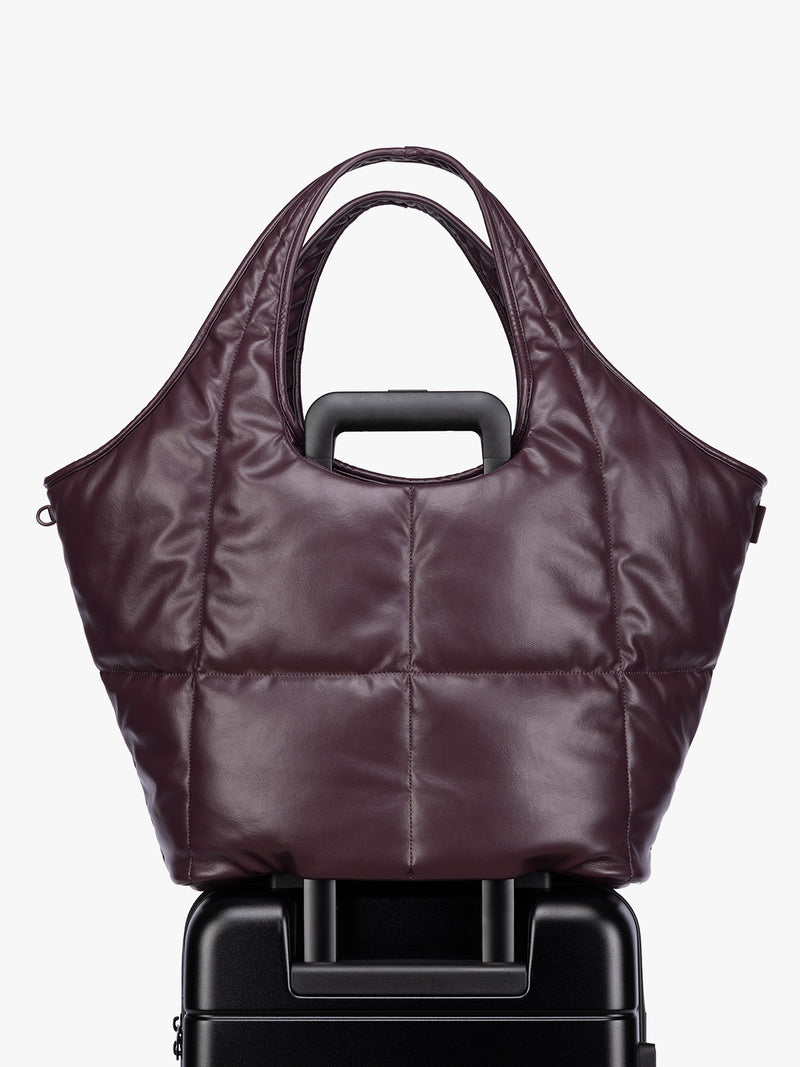 Luggage trolley sleeve of the Dark Cherry quilted puffer CALPAK Luka Everything Tote Bag with a smooth finish and double shoulder straps, shown against a plain white background