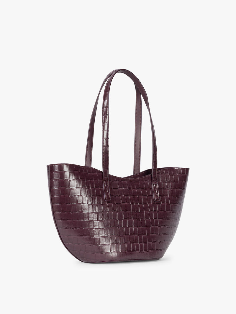 Side view of a CALPAK Haven Tulip Tote in Dark Cherry dark plum purple crocodile-embossed leather tote bag with double shoulder straps  against a plain white background