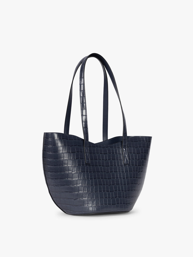 Side view of a navy blue crocodile-embossed CALPAK Haven Tulip tote bag with double shoulder straps against a plain white background