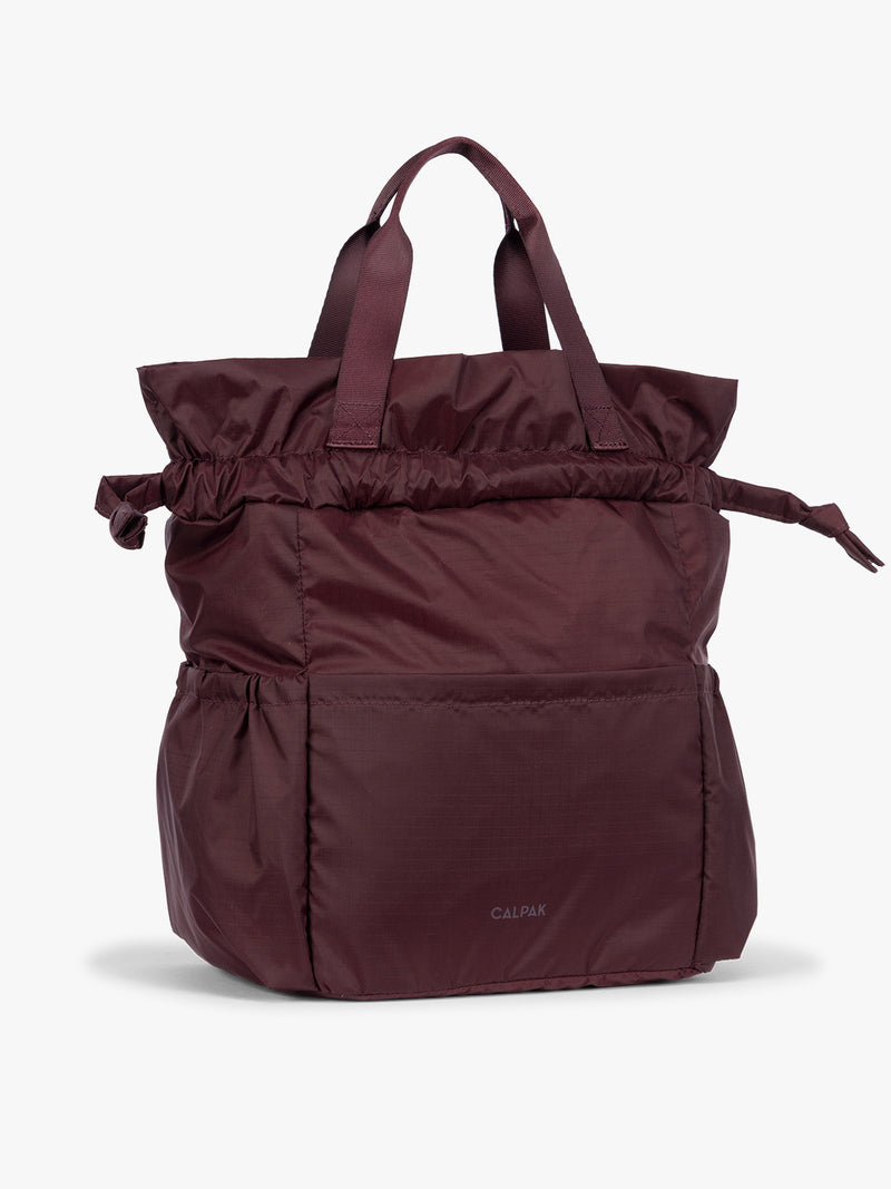 Dark Cherry burgundy CALPAK Insulated Lunch Bag with top handles, featuring an expandable function shown against a plain white background