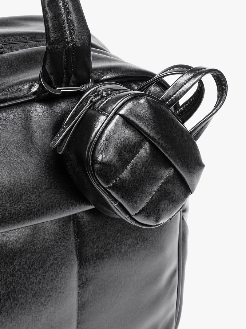 A close-up of a Black vegan leather top-handle CALPAK Luka Zip Bag Charm with a zippered front pocket and a small side strap  with a matching small zippered pouch attached near the handle, shown against a clean white background