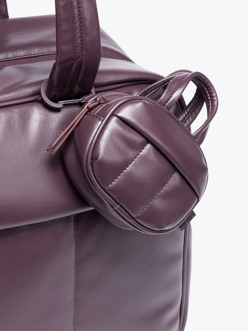 A close-up of a deep burgundy Dark Cherry vegan leather top-handle CALPAK Luka Zip Bag Charm with a zippered front pocket and a small side strap  with a matching small zippered pouch attached near the handle, shown against a clean white background