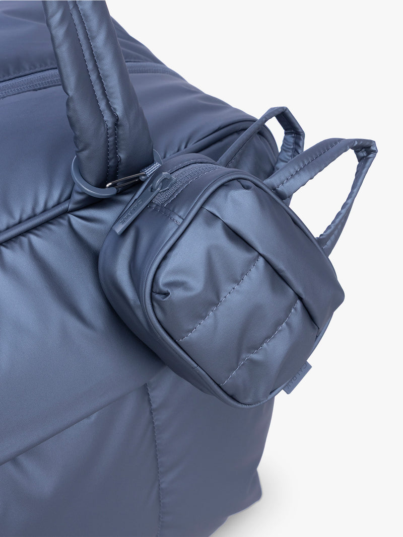 CALPAK Luka Duffel Zip Bag Charm in dark blue metallic material in Metallic Indigo clipped on a bag