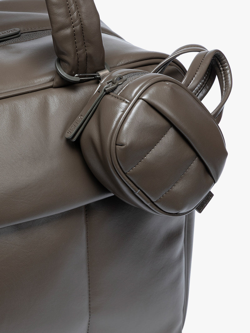 A close-up of a dark brown Mushroom vegan leather top-handle CALPAK Luka Zip Bag Charm with a zippered front pocket and a small side strap  with a matching small zippered pouch attached near the handle, shown against a clean white background