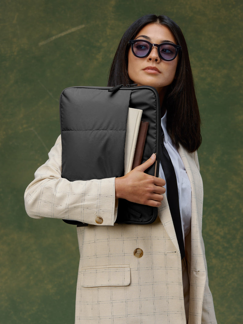 Model holding black CALPAK Luka 14 inch Laptop Backpack right hand with notebooks in front pocket of padded laptop sleeve