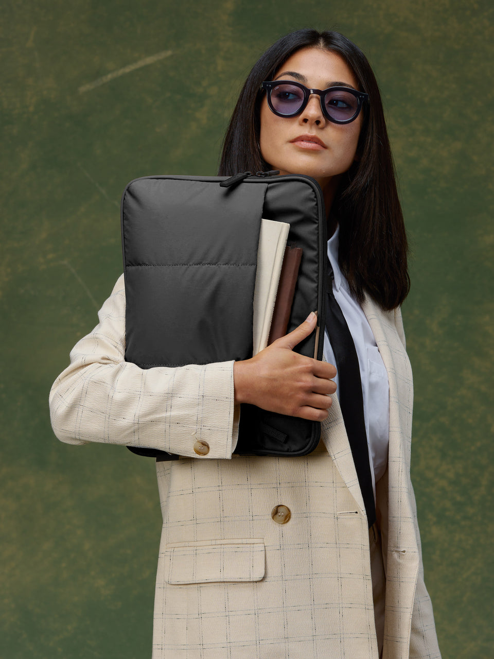 Model holding black CALPAK Luka 14 inch Laptop Backpack right hand with notebooks in front pocket of padded laptop sleeve; ALL2401-MATTE-BLACK