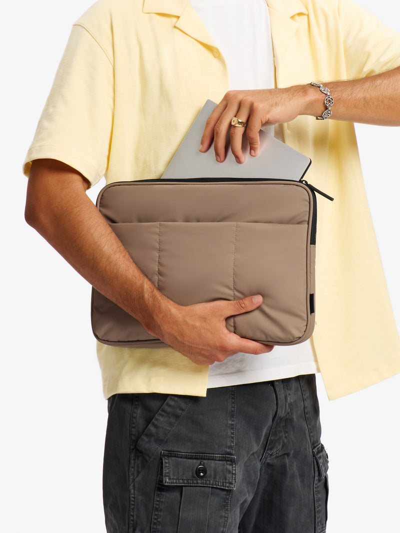 Model placing 14 inch laptop into main pocket of CALPAK Luka 14" Padded Laptop Sleeve in chocolate brown