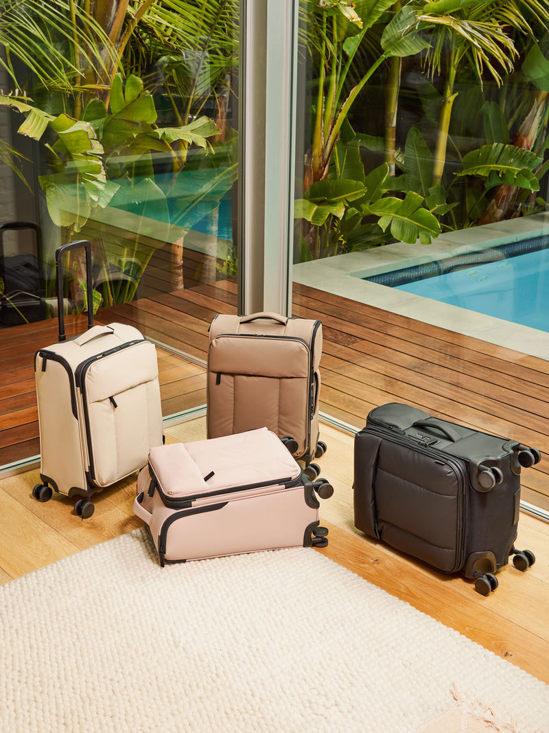 CALPAK white, brown, pink, and black Luka Soft-Sided Carry On by a pool and rug. 