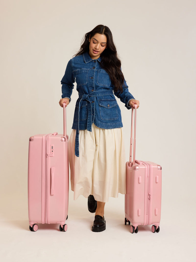 Model with CALPAK 2pc Ambeur Luggage Set featuring the Ambeur Carry-On Luggage and Ambeur Large Luggage in metallic pink Blossom with pink wheels