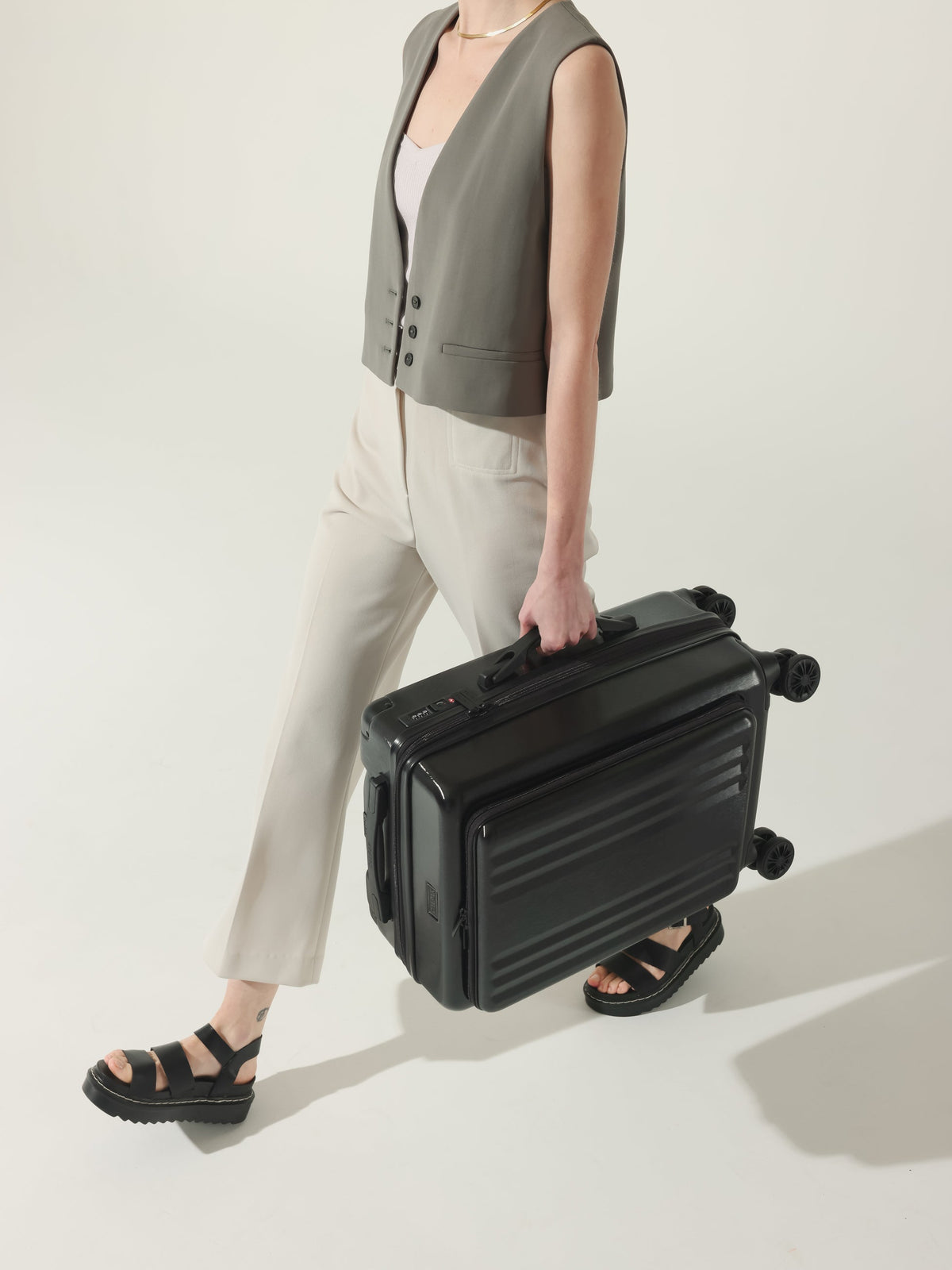 Model carrying CALPAK Ambeur hard shell carry-on with front pocket, cushioned top and side handles in black; LAM1020-FP-BLACK