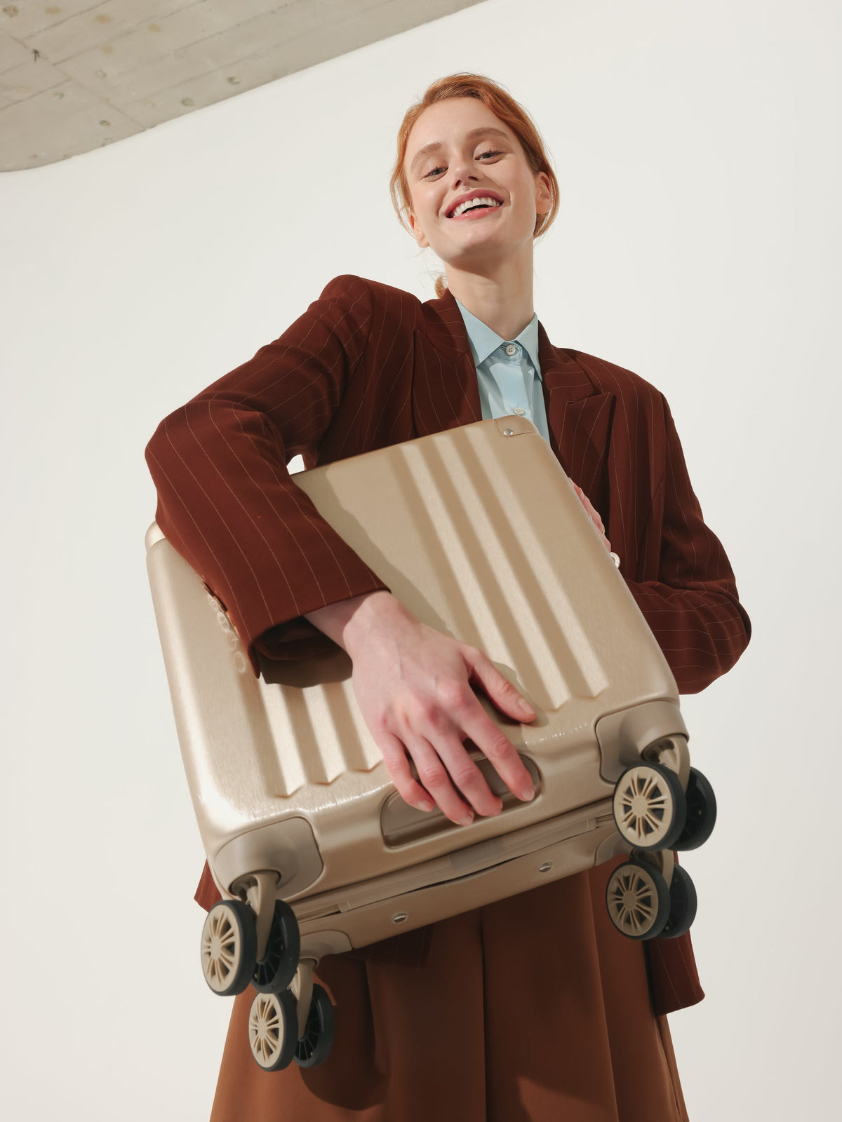 Model carrying CALPAK Ambuer small carry on luggage with wheels and cushioned top and side handles in gold; LAM1014-GOLD