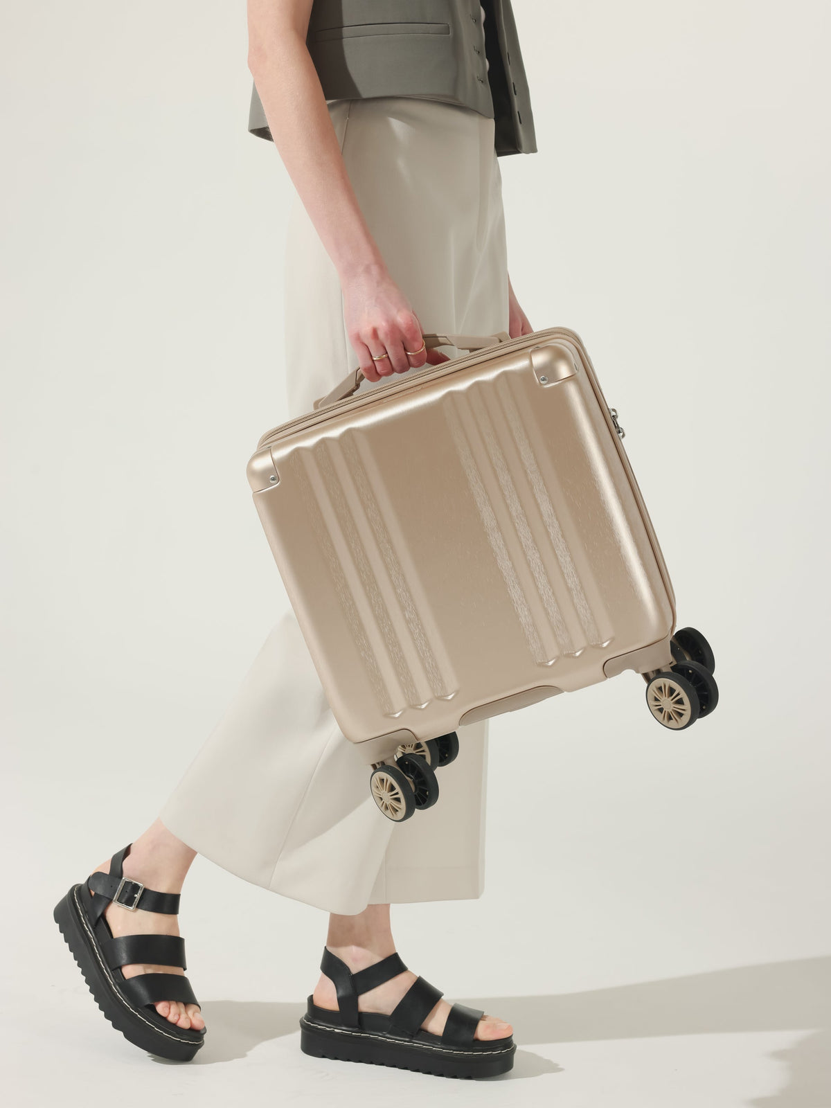 Model carrying CALPAK Ambuer 16 inch carry-on luggage with wheels and cushioned top and side handles in gold; LAM1014-GOLD